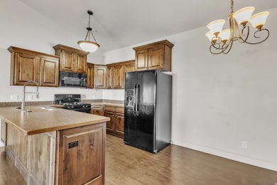 Kitchen with a peninsula, black appliances, brown cabinetry, light wood-style flooring, and light countertops