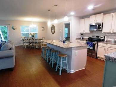 Kitchen with appliances with stainless steel finishes, a sink, dark wood-style flooring, light stone counters, and white cabinets