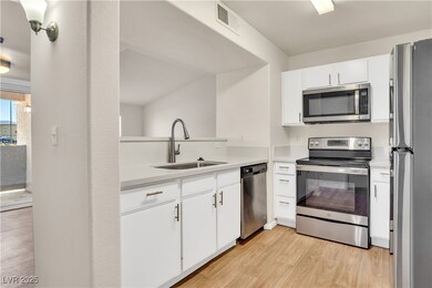 Kitchen featuring stainless steel appliances, white cabinets, light wood-style flooring, and light stone counters