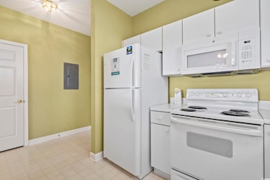 Kitchen featuring white appliances, white cabinetry, electric panel, light countertops, and a textured ceiling