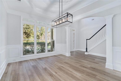 Unfurnished dining area featuring arched walkways, decorative columns, stairs, crown molding, and light wood-style floors