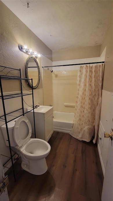 Full bathroom featuring vanity, shower / bathtub combination with curtain, dark wood-type flooring, and a textured wall
