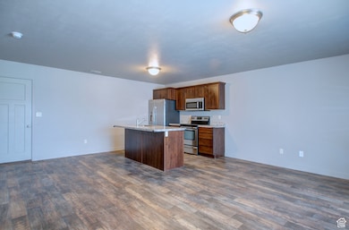Kitchen featuring open floor plan, appliances with stainless steel finishes, a kitchen island, dark wood-style floors, and brown cabinets