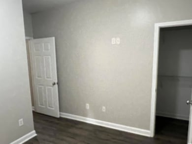 Unfurnished bedroom featuring dark wood-type flooring, baseboards, and a spacious closet