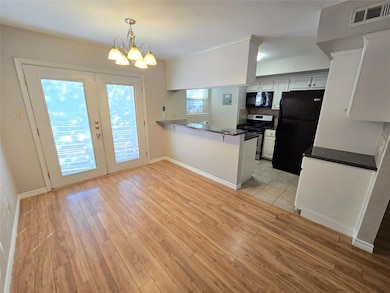 Kitchen featuring black appliances, white cabinets, a peninsula, pendant lighting, and french doors