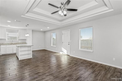 Unfurnished living room with dark wood-type flooring, a raised ceiling, and ceiling fan