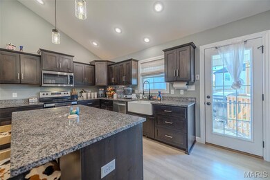 Kitchen featuring dark brown cabinetry, dark stone countertops, vaulted ceiling, light wood finished floors, and appliances with stainless steel finishes