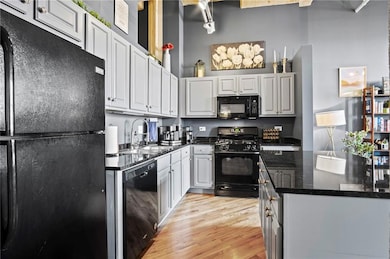 Kitchen featuring light wood-style flooring, white cabinets, a sink, dark stone counters, and black appliances