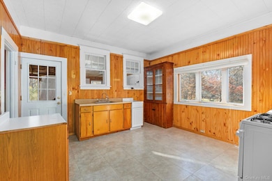Kitchen with wood walls, light countertops, brown cabinets, white gas stove, and light tile patterned floors