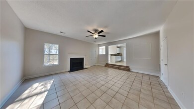 Unfurnished living room featuring a fireplace with flush hearth, ceiling fan, light tile patterned floors, baseboards, and a textured ceiling