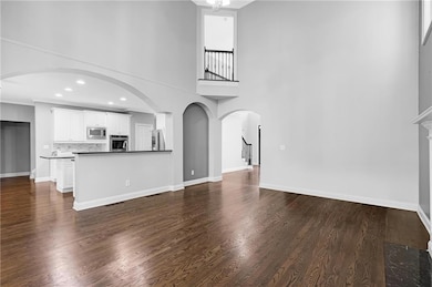 Unfurnished living room with dark wood-type flooring, a towering ceiling, and stairs