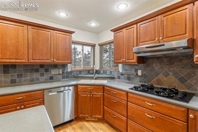 Kitchen with dishwasher, black gas cooktop, under cabinet range hood, light wood finished floors, and brown cabinetry