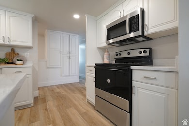 Kitchen featuring stainless steel appliances, white cabinetry, recessed lighting, light wood-style flooring, and light stone countertops
