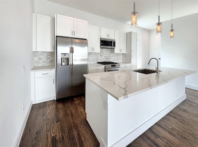 Kitchen with stainless steel appliances, white cabinetry, light stone countertops, backsplash, and pendant lighting