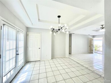 Unfurnished room with a raised ceiling, french doors, a healthy amount of sunlight, and ceiling fan with notable chandelier