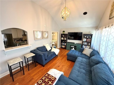 Living area featuring an inviting chandelier, arched walkways, high vaulted ceiling, and wood finished floors
