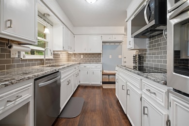 Kitchen featuring stainless steel appliances, white cabinets, dark wood-style floors, light stone counters, and tasteful backsplash