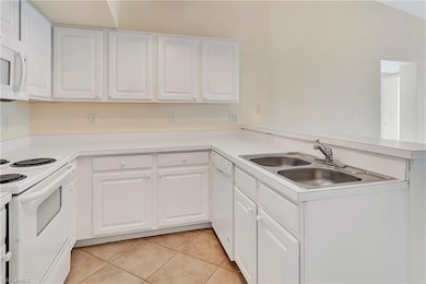 Kitchen featuring white cabinets, light tile patterned floors, white appliances, and kitchen peninsula