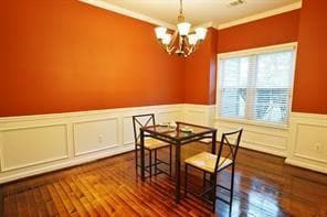 Dining room featuring a wainscoted wall, a chandelier, a decorative wall, ornamental molding, and dark wood-type flooring