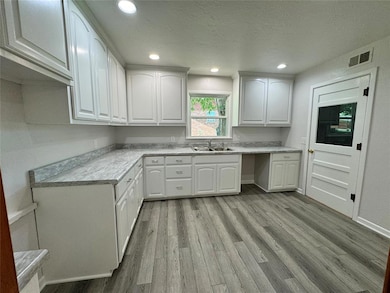 Kitchen featuring white cabinets, sink, light hardwood / wood-style flooring, and a textured ceiling