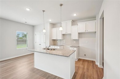 Kitchen with white cabinetry, light wood-style flooring, tasteful backsplash, light stone countertops, and hanging light fixtures