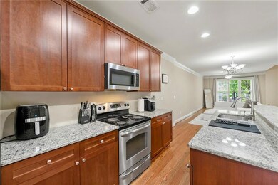 Kitchen with appliances with stainless steel finishes, a chandelier, light wood-type flooring, light stone counters, and crown molding