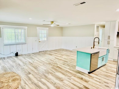 Kitchen featuring light hardwood / wood-style flooring, a center island with sink, sink, stainless steel dishwasher, and white cabinetry