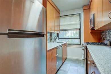 Kitchen featuring stainless steel appliances, decorative backsplash, light stone counters, light tile patterned flooring, and brown cabinetry