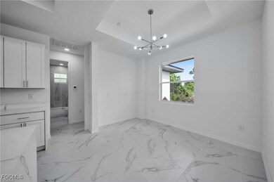 Unfurnished dining area featuring plenty of natural light, light marble finish floors, a chandelier, and a tray ceiling