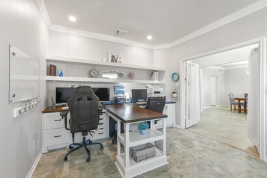 Opposite the dining room, a pair of French doors open into this private study that features crown molding, recessed lighting, tile floors, a pair of front-facing windows, and a built-in dual desk station with drawers,  shelving, and a center peninsula.
