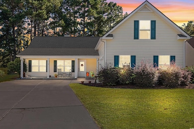 Traditional-style house with a yard, covered porch, driveway, and a shingled roof