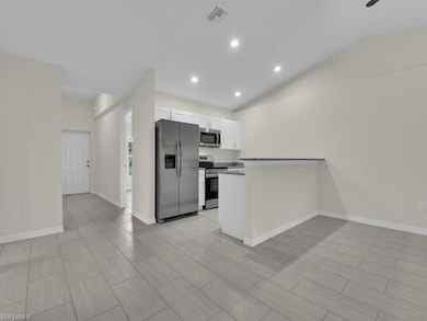 Kitchen featuring stainless steel appliances, white cabinets, vaulted ceiling, recessed lighting, and a peninsula
