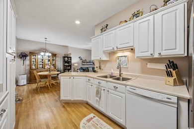 Kitchen with white dishwasher, a sink, light countertops, white cabinets, and light wood-style flooring