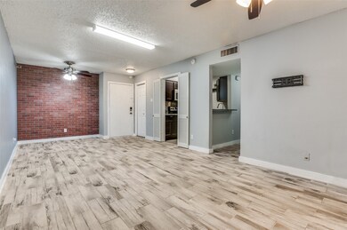 Unfurnished room with a ceiling fan, brick wall, light wood-type flooring, and a textured ceiling