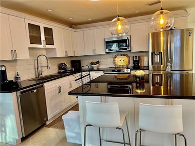 Kitchen with appliances with stainless steel finishes, white cabinets, a kitchen bar, tasteful backsplash, and light tile patterned floors