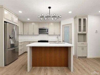 Kitchen with an island with sink, a sink, light wood-style flooring, appliances with stainless steel finishes, and a notable chandelier