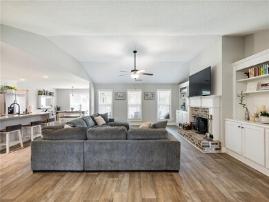 Living room with vaulted ceiling, healthy amount of natural light, a ceiling fan, wood finished floors, and a brick fireplace