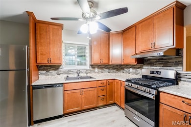 Kitchen with appliances with stainless steel finishes, brown cabinets, backsplash, and under cabinet range hood