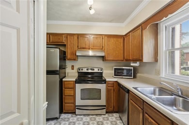 Kitchen featuring appliances with stainless steel finishes, light countertops, brown cabinets, crown molding, and under cabinet range hood