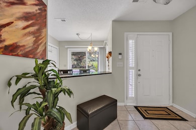 Foyer with healthy amount of natural light, tile patterned flooring, a chandelier, baseboards, and a textured ceiling