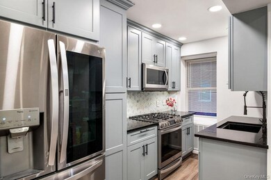 Kitchen featuring stainless steel appliances, dark stone counters, decorative backsplash, gray cabinets, and light wood-type flooring