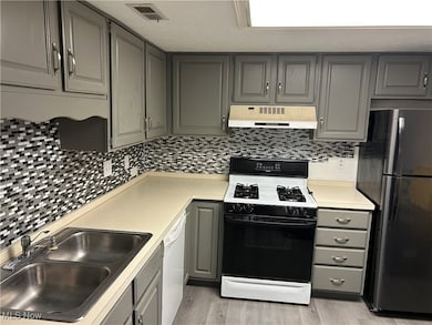 Kitchen with gray cabinetry, range with gas cooktop, freestanding refrigerator, and decorative backsplash