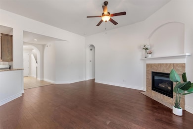 Unfurnished living room with dark wood-type flooring, a tiled fireplace, and ceiling fan