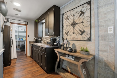 Kitchen featuring dark wood-type flooring, dark countertops, backsplash, dark brown cabinetry, and freestanding refrigerator