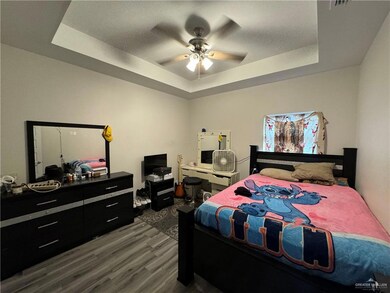 Bedroom with a tray ceiling, dark wood-style floors, and ceiling fan