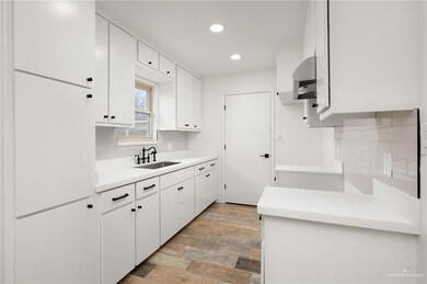 Kitchen featuring white cabinetry, wall chimney exhaust hood, sink, and tasteful backsplash