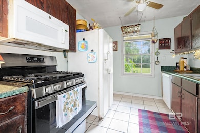 Kitchen featuring white appliances, dark countertops, light tile patterned floors, and dark brown cabinets