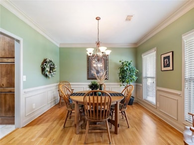 Dining space featuring light wood-style flooring, wainscoting, a chandelier, a decorative wall, and crown molding