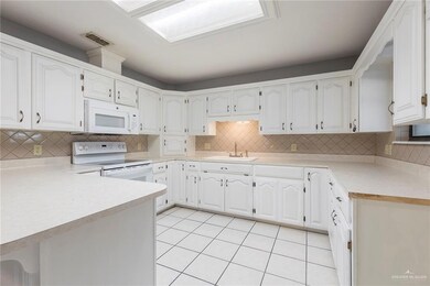 Kitchen with white appliances, decorative backsplash, light tile patterned flooring, a sink, and white cabinets
