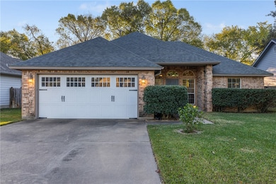 View of front of property with a front yard, brick siding, a shingled roof, concrete driveway, and a garage